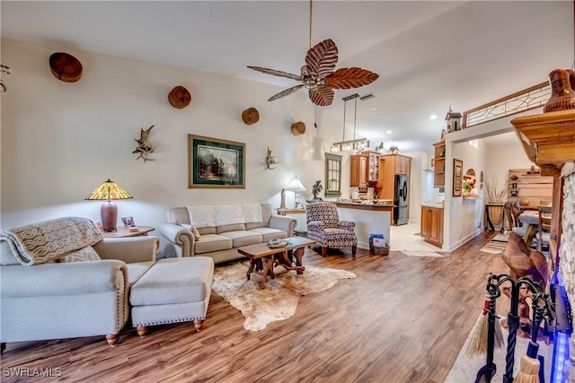 living room featuring a stone fireplace, ceiling fan, and light hardwood / wood-style flooring