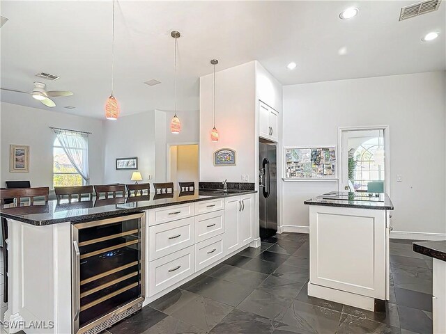 kitchen featuring stainless steel refrigerator with ice dispenser, beverage cooler, ceiling fan, white cabinetry, and hanging light fixtures