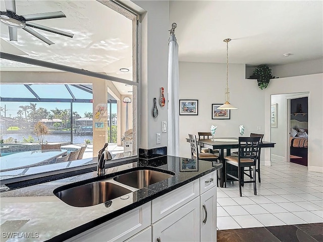 kitchen featuring dark stone counters, sink, a water view, white cabinets, and hanging light fixtures