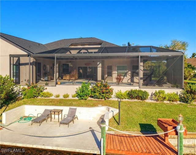 rear view of house with glass enclosure, ceiling fan, a patio area, and a lawn