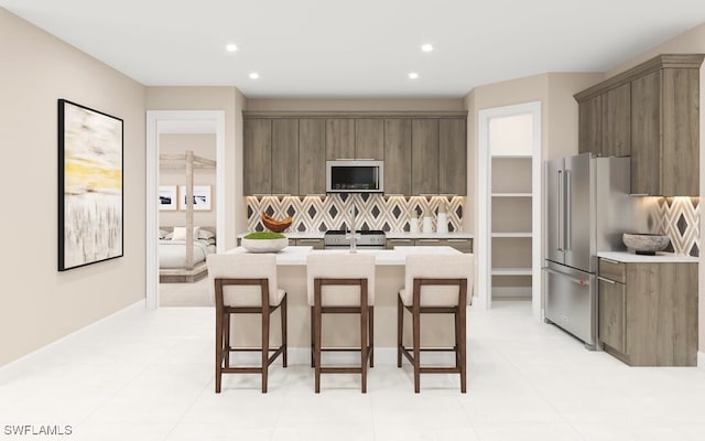 kitchen featuring backsplash, a kitchen island with sink, a breakfast bar area, and high end appliances