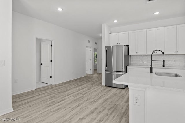 kitchen featuring white cabinets, a sink, freestanding refrigerator, and decorative backsplash