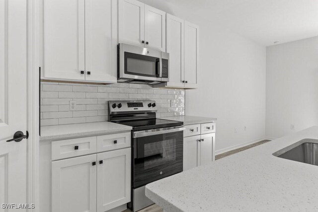 kitchen featuring white cabinetry, baseboards, appliances with stainless steel finishes, light stone countertops, and tasteful backsplash