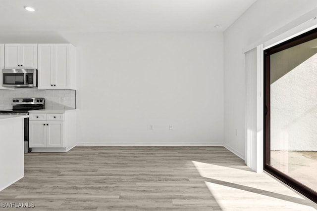 kitchen with appliances with stainless steel finishes, white cabinets, light wood-style floors, and backsplash