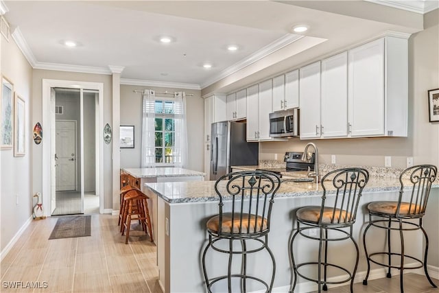 kitchen with a breakfast bar, ornamental molding, appliances with stainless steel finishes, light stone counters, and white cabinetry