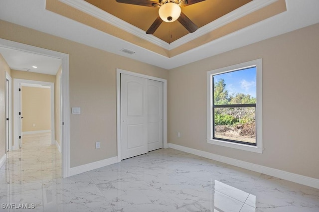 unfurnished bedroom with ceiling fan, a closet, ornamental molding, and a tray ceiling