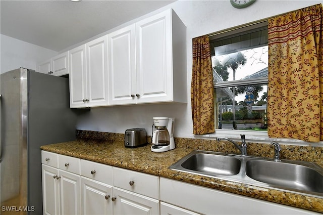 kitchen with dark stone counters, white cabinetry, stainless steel refrigerator, and sink