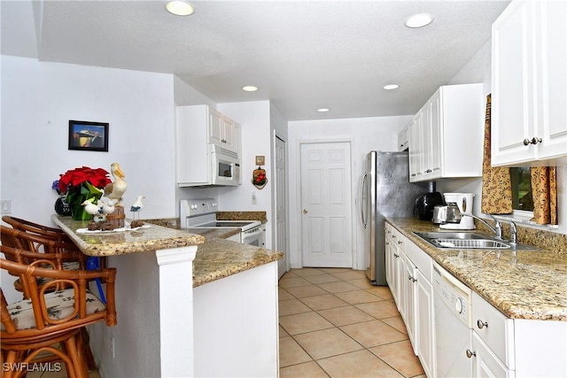 kitchen featuring sink, kitchen peninsula, white appliances, a kitchen bar, and white cabinets