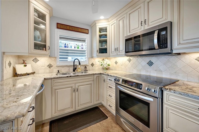 kitchen featuring backsplash, sink, light stone countertops, appliances with stainless steel finishes, and light tile patterned flooring