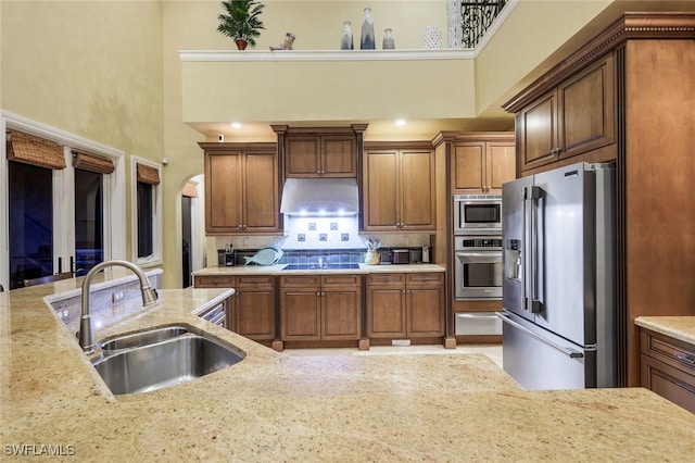 kitchen with light stone countertops, a towering ceiling, stainless steel appliances, and sink