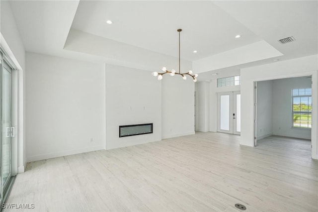 unfurnished living room featuring light hardwood / wood-style floors, an inviting chandelier, a tray ceiling, and french doors