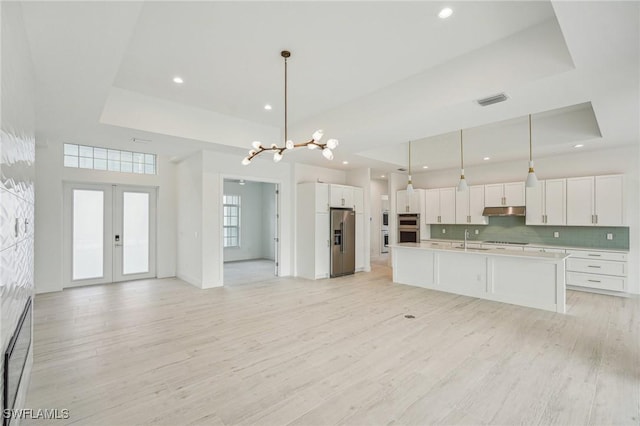 kitchen featuring a tray ceiling, pendant lighting, stainless steel appliances, and light wood-type flooring