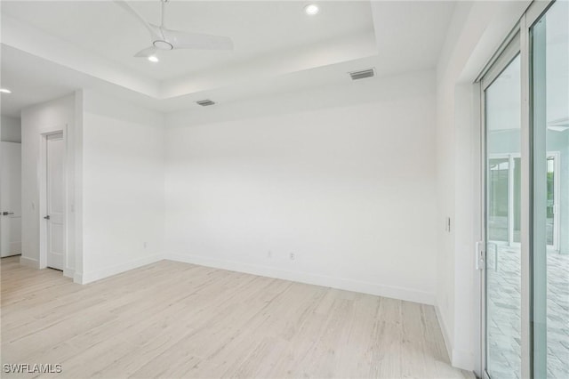 unfurnished room with ceiling fan, light hardwood / wood-style floors, and a tray ceiling