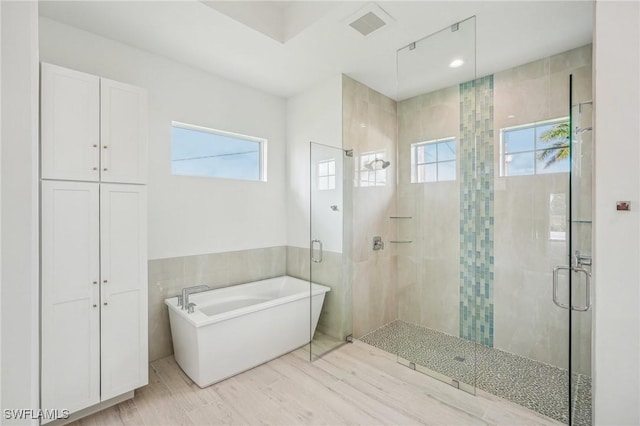 bathroom with a wealth of natural light, hardwood / wood-style floors, independent shower and bath, and tile walls