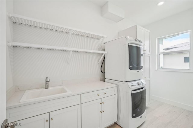 washroom featuring stacked washer / dryer, sink, cabinets, and light wood-type flooring