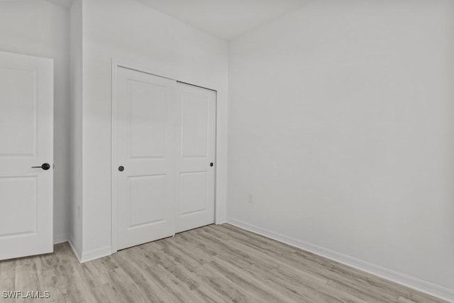 unfurnished bedroom featuring light wood finished floors, a closet, and baseboards