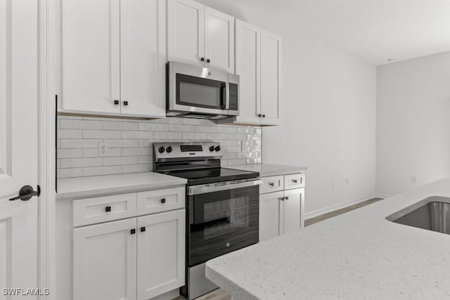 kitchen with baseboards, light stone counters, stainless steel appliances, white cabinetry, and backsplash