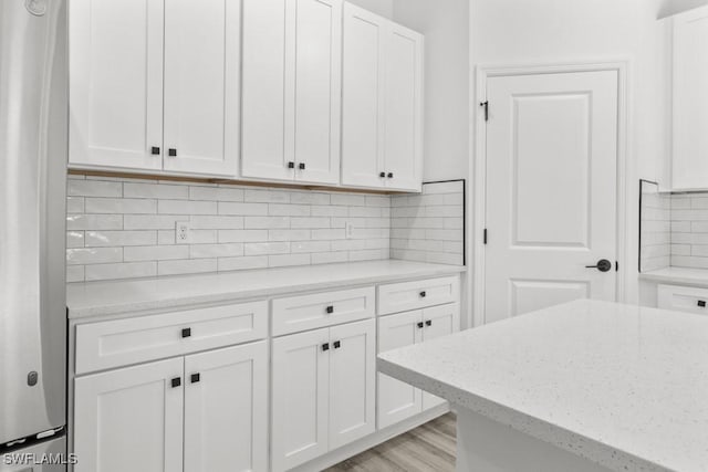 kitchen with light stone countertops, white cabinetry, decorative backsplash, and stainless steel refrigerator