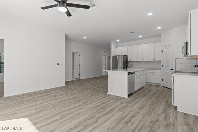 kitchen with stainless steel appliances, open floor plan, light wood-style floors, and decorative backsplash