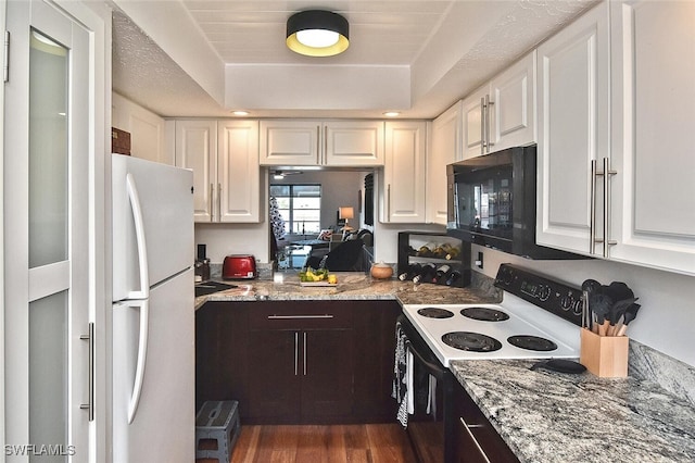 kitchen featuring a raised ceiling, black microwave, freestanding refrigerator, white cabinetry, and range with electric stovetop