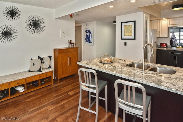 kitchen with a sink, freestanding refrigerator, a breakfast bar area, light stone countertops, and dark wood finished floors