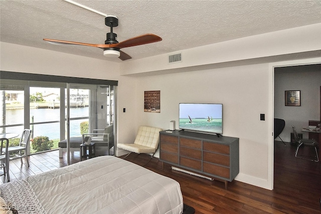 bedroom featuring wood finished floors, a textured ceiling, baseboards, visible vents, and a water view