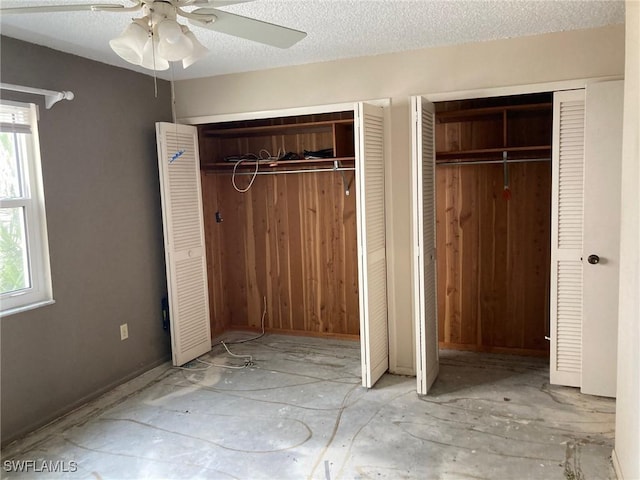 unfurnished bedroom featuring multiple windows, a textured ceiling, ceiling fan, and multiple closets