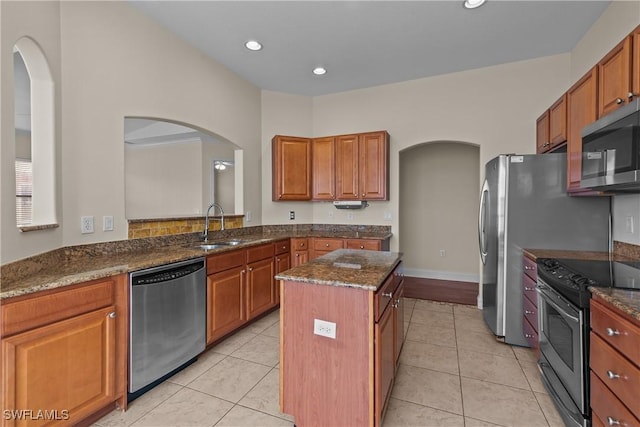 kitchen featuring a center island, dark stone counters, sink, light tile patterned floors, and appliances with stainless steel finishes