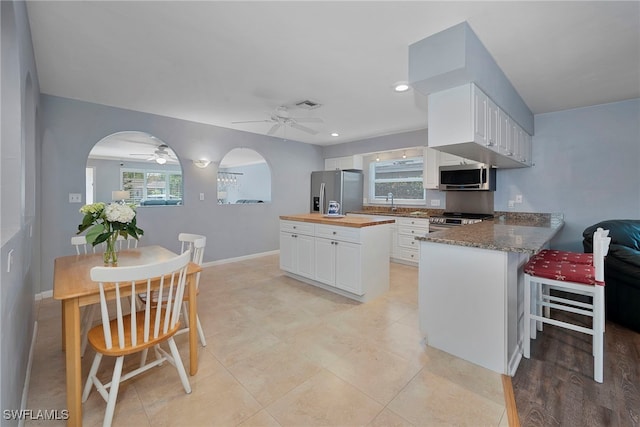 kitchen featuring arched walkways, a peninsula, appliances with stainless steel finishes, and white cabinets