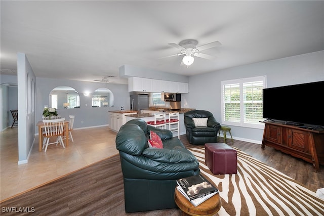 living room featuring baseboards, arched walkways, and a ceiling fan