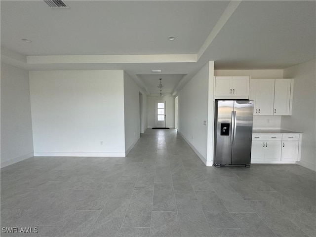 kitchen with a raised ceiling, stainless steel fridge, white cabinets, and light tile patterned flooring