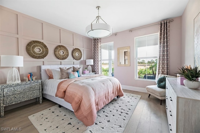 bedroom featuring baseboards, light wood finished floors, and a decorative wall