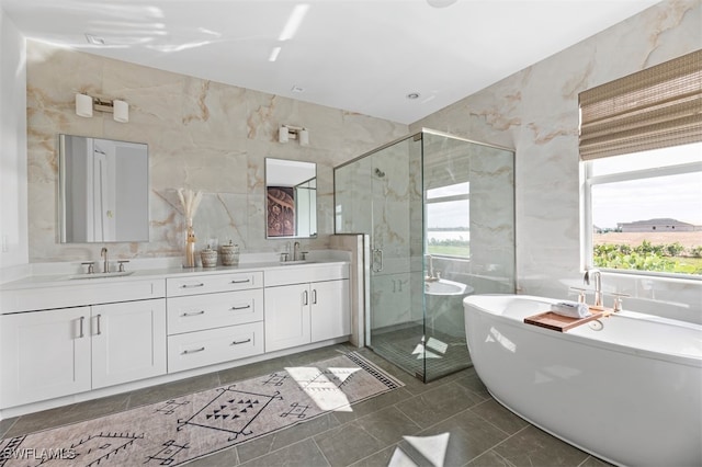 bathroom with double vanity, tile walls, a freestanding tub, a shower stall, and a sink