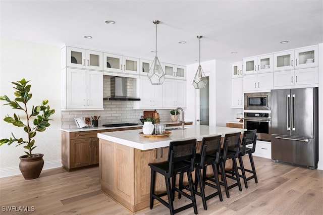 kitchen with tasteful backsplash, wall chimney exhaust hood, appliances with stainless steel finishes, light wood-style floors, and a sink