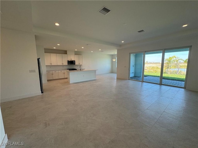 kitchen with a sink, visible vents, white cabinetry, open floor plan, and stainless steel microwave