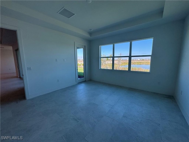 unfurnished room featuring a tray ceiling, visible vents, and a water view