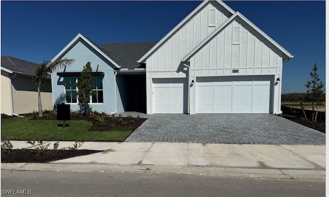 modern farmhouse style home with an attached garage, decorative driveway, a front lawn, and board and batten siding