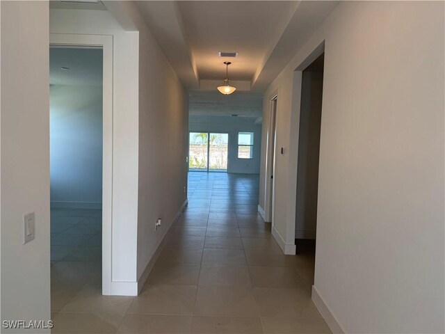 hallway with a raised ceiling and light tile patterned floors