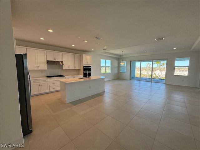 kitchen with open floor plan, under cabinet range hood, black cooktop, a sink, and freestanding refrigerator