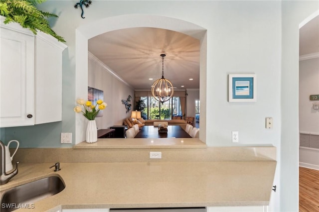 kitchen with ornamental molding, sink, an inviting chandelier, hardwood / wood-style floors, and white cabinetry