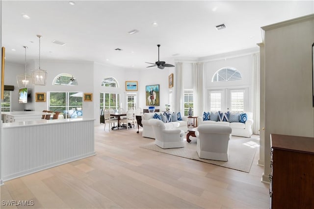 living room with ceiling fan with notable chandelier, a high ceiling, crown molding, and light wood-type flooring