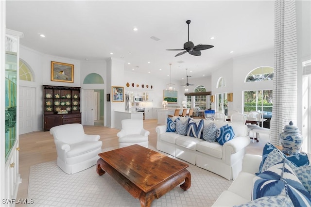 living room with ceiling fan, a high ceiling, crown molding, and light wood-type flooring