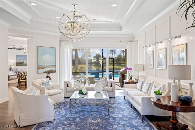 living room with a raised ceiling, crown molding, hardwood / wood-style floors, and ceiling fan with notable chandelier