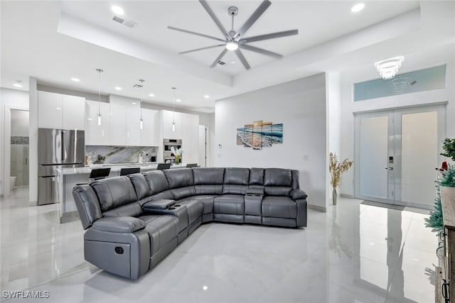 living room featuring a raised ceiling and ceiling fan with notable chandelier