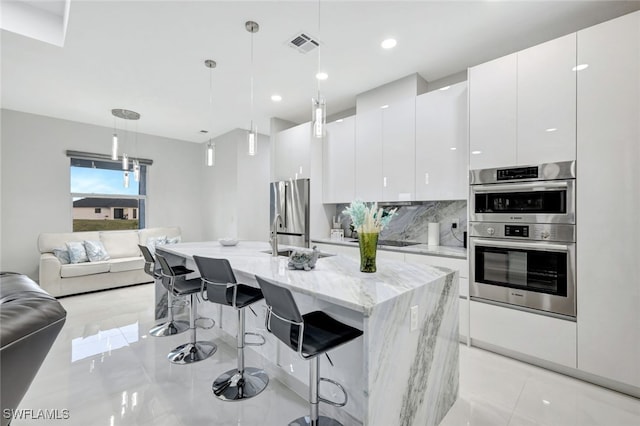 kitchen featuring white cabinets, a kitchen bar, decorative light fixtures, and stainless steel appliances