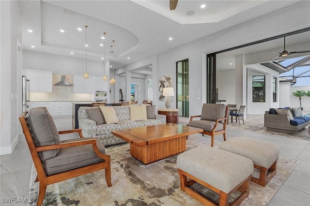 living room with ceiling fan, a raised ceiling, and plenty of natural light