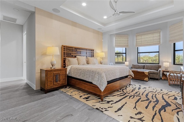 bedroom with a raised ceiling, multiple windows, and ceiling fan