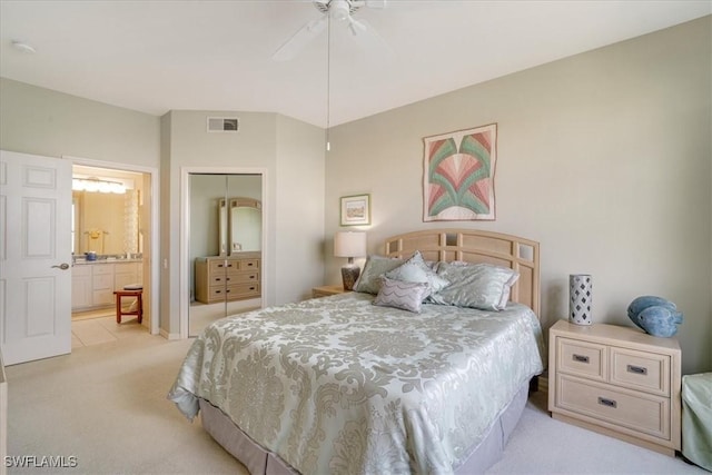 bedroom featuring light carpet, a closet, ensuite bath, and ceiling fan