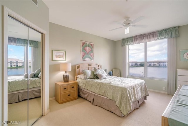 bedroom featuring ceiling fan, a closet, a water view, and light carpet