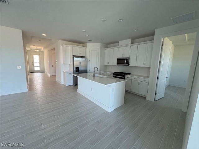 kitchen with sink, a center island with sink, light wood-type flooring, stainless steel appliances, and white cabinets